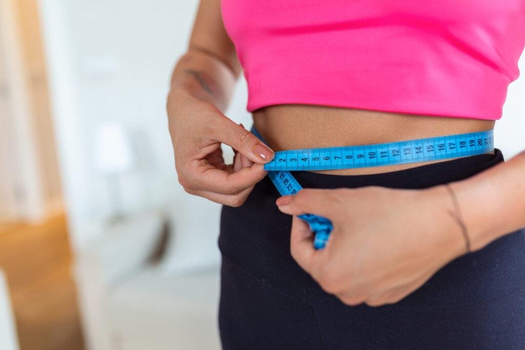Femme mesurant son tour de taille avec un ruban métrique bleu après une perte de poids.