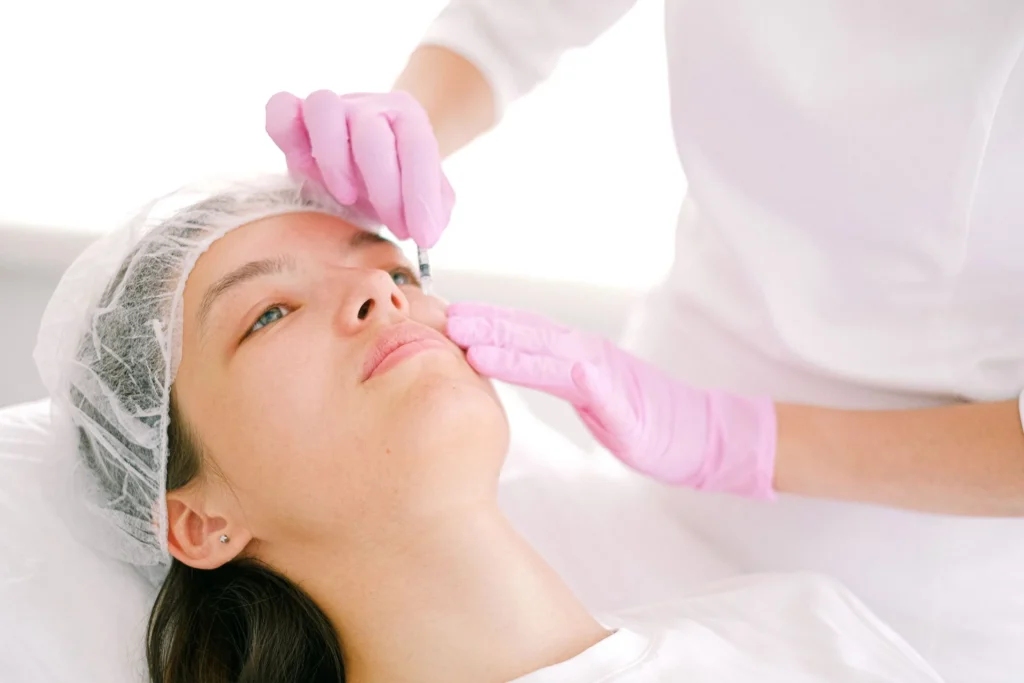 Praticienne en gants roses réalisant une injection d'acide hyaluronique sur le visage d'une patiente